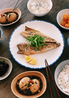 a table topped with plates and bowls filled with different types of food next to chopsticks