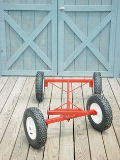 a red cart with four wheels on a wooden floor next to a blue garage door