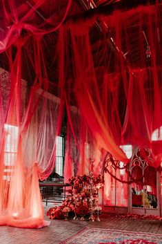 a room with red sheer curtains and flowers on the floor