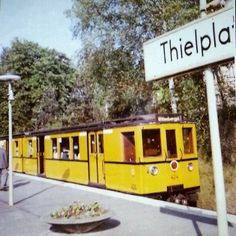 a yellow train traveling down tracks next to a street sign with people standing on it