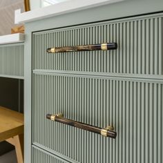 a green dresser with brass handles and knobs next to a wooden table in a room