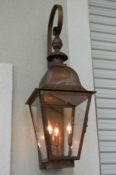 three lit candles are attached to the side of a wall light on a white building