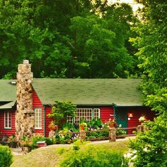 a red house surrounded by lush green trees and bushes in the foreground is a stone chimney