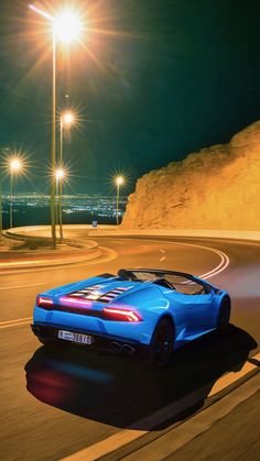 a blue sports car driving on a road at night time with street lights in the background