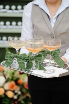 the waiter is holding three glasses of wine on a silver tray with green bow ties