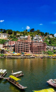 several small boats floating on top of a river next to a large city with lots of buildings