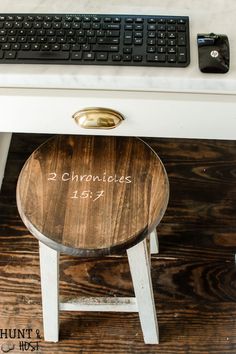 a wooden stool sitting next to a computer keyboard on top of a white desk with writing on it