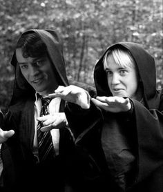 two people dressed in robes and holding out their hands to the camera, with trees in the background