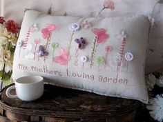 two pillows with flowers on them sitting next to a cup and flower vase in front of the pillow