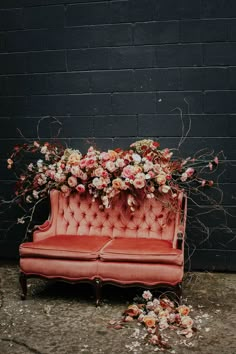 an old pink couch with flowers on it and vines growing out of the back, in front of a brick wall