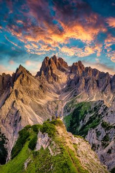 the mountains are covered in green grass and some clouds at sunset, with bright colors on them