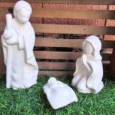 two white statues sitting on top of green grass next to a wooden crate with wood slats in the background