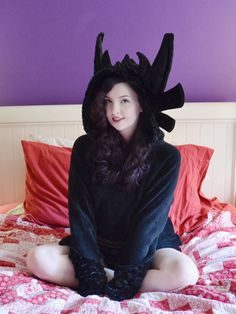 a woman sitting on top of a bed wearing a black devil costume with horns and wings