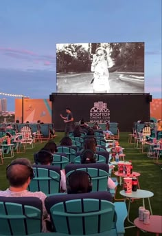 people sitting in lawn chairs watching a movie on the screen at an outdoor event or gathering