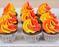 cupcakes decorated with orange and yellow frosting on a white platter, ready to be eaten