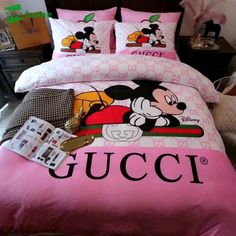 a bed with pink comforter and mickey mouse pillow cases on it, along with other items