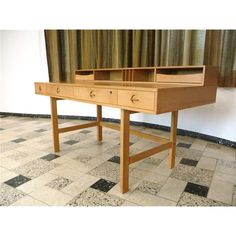 a wooden desk with two drawers sitting on top of a checkered floor next to a window