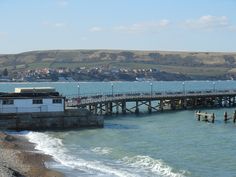 a pier on the water with buildings in the background and people walking along it near the shore