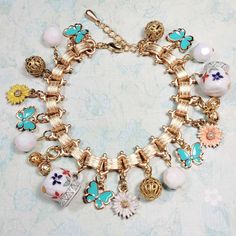 This pretty bracelet is made with colorful charms and vintage beads. Enameled butterflies and flowers combine with adorable porcelain pitcher charms to create a breezy summer theme. Vintage brass filigree and acrylic beads accent the look. This bracelet has a quality matte gold plated Victorian style book chain that closes with a lobster clasp. The length is adjustable to 7-1/2 to 8-3/4 inches long. ✨ Note: I do my best to take accurate photos. Please be aware that colors and brightness can vary Bracelet Flowers, Handmade Charm Bracelets, Butterfly Charm Bracelet, Theme Vintage, Porcelain Pitcher, Brass Filigree, Butterflies And Flowers, Cow Painting, Flowers And Butterflies