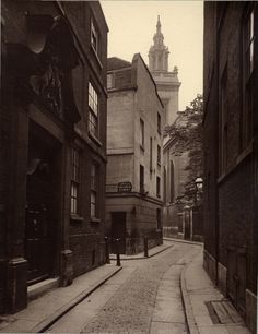 an old black and white photo of a narrow city street with buildings on both sides