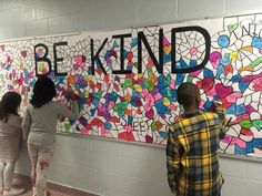 three people standing in front of a wall that says be kind