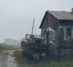 an old boat sitting on the side of a dirt road next to a wooden building