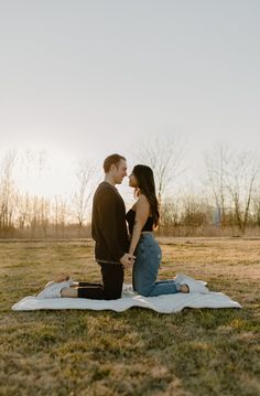 a man and woman sitting on top of a blanket in the middle of a field