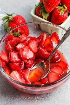 strawberries in a glass bowl with a spoon and another bowl full of strawberries