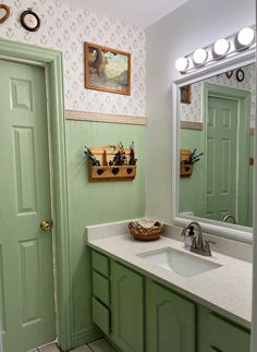 a bathroom with green cabinets and a white sink under a large mirror on the wall