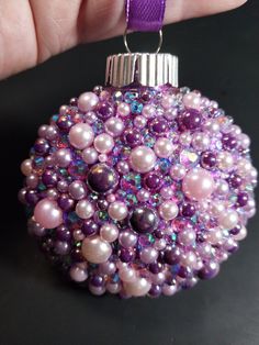 a hand holding a purple ornament with pearls on it