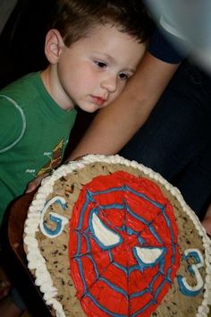 a young boy is looking at a spiderman cake