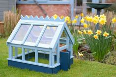 a small blue house sitting in the grass next to daffodils