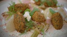 a white plate topped with meatballs and veggies covered in sauce on top of lettuce