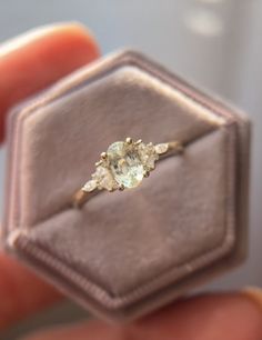 a ring with three stones in it sitting on top of a velvet box that is held by someone's hand