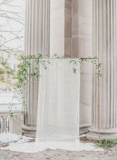 an outdoor ceremony setup with white linen and greenery on the ground, surrounded by columns