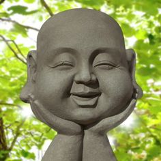 a statue of a smiling buddha with his eyes closed and hands behind his head, in front of green leaves