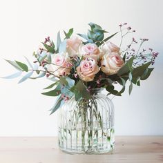 a vase filled with pink roses and greenery