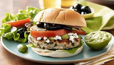 a chicken burger with lettuce, tomatoes and olives on a blue plate