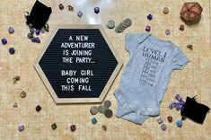 a baby's bodysuit and other items are on the floor next to a sign that says, a new adventure is joining the party