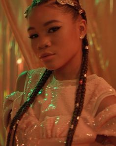 a woman with long braids wearing a white shirt and green sequins on her hair