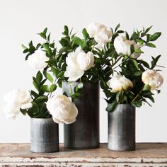 three vases filled with white flowers sitting on top of a wooden table next to each other