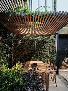 an outdoor dining area with wooden table and chairs, surrounded by greenery on either side