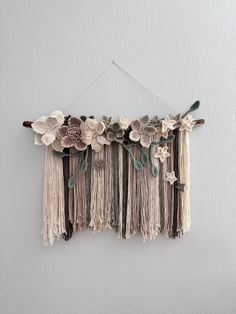 a wall hanging with flowers and tassels attached to the side on a white wall