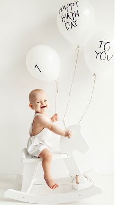 a baby sitting on a rocking horse with balloons