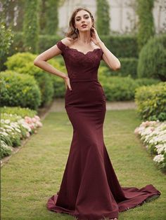 a woman in a long maroon dress posing for the camera with her hands on her head