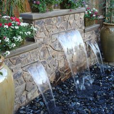 three water fountains in front of a stone wall