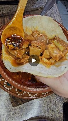 a person holding a tortilla with meat and sauce on it in a bowl