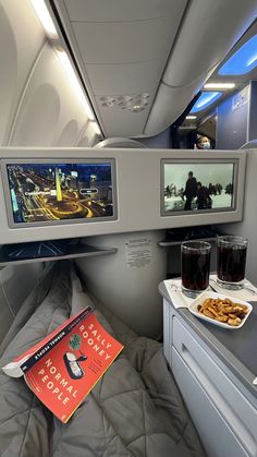 the interior of an airplane with food and drinks on it, along with a book