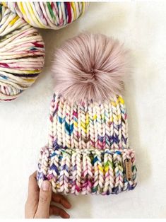 a hand is holding a multicolored knitted beanie with a pom - pom