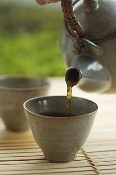 a person pouring tea into a cup on a table with two bowls in the background